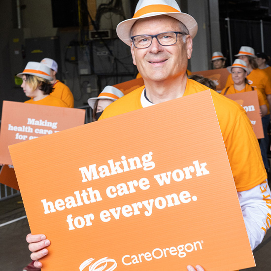 Group of people in orange attire holding signs that read ‘Making health care work for everyone. CareOregon,’ in a parade.