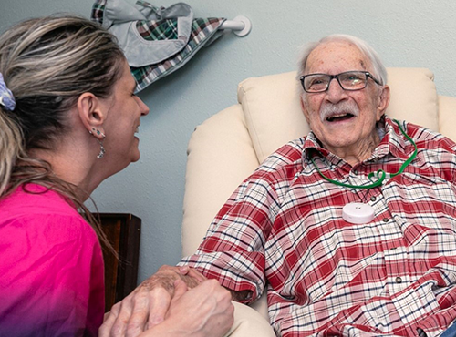 A Housecall Providers Hospice patient smiles and holds hands with a member of his care team.